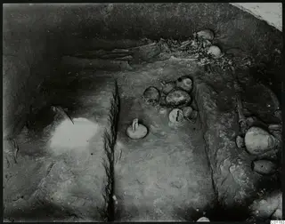 Interior of Tomb 7 at Kountoura Trachonia, with skulls and bones against the back wall and pottery vessels on the floor.