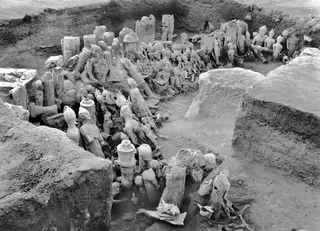 Excavated pit at Ayia Irini with many terracotta figurines and sculptures lying in front of a large drum-shaped block