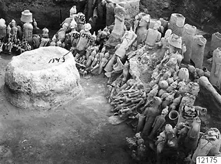 Excavated figures and statue fragments heaped beside a round stone altar at Ayia Irini