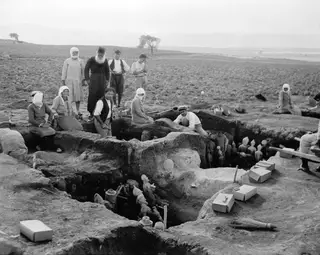 Excavation at Ayia Irini, with people standing and crouching around a trench holding clay figurines and jars.