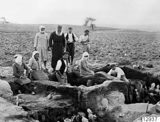 Papa Prokopios inspects excavation work at Ayia Irini, with people gathered at the edge of a trench