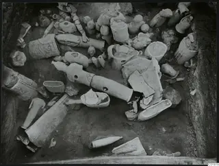 Excavation at Ayia Irini showing broken figure fragments and vessels lying in situ in the trench