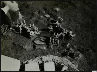 Small pale figurines and wheeled stands lying in the ground during excavation at Ayia Irini.