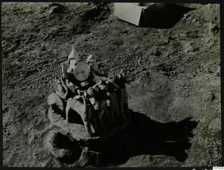Modelled clay object with animal forms and a round disc on top, lying in excavation soil at Ayia Irini