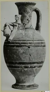 Tall painted vessel with a strap handle and a modelled human figure on the shoulder, against a plain background