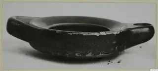 Black glazed two-handled bowl seen from the side against a pale background