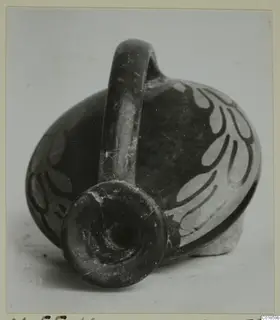 Dark pottery vessel with a strap handle and pale painted leaf motifs, shown from the spout end