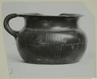Black-glazed pottery vessel with a loop handle, reeded bands and stamped rosettes, photographed from the side