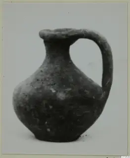 Black Slip juglet from Marion with a single strap handle, shown on a pale surface.