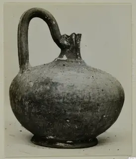 Round-bodied jug with a tall loop handle and a broken, flared neck, photographed on a plain background.