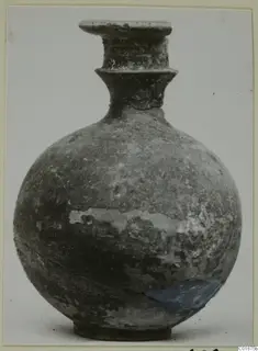 Round-bodied jug with a tall flared neck and rim, dark worn surface, shown against a plain background.