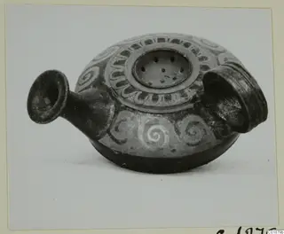 Dark pottery vessel with white spiral painting, a flared spout and a perforated disc on its top