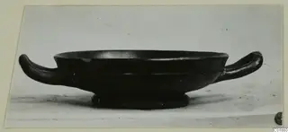 Black glazed two-handled kantharos, side view, on a pale surface
