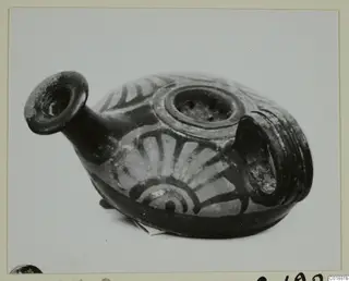 Strainer-spouted vessel with a flared spout, a perforated top opening and a ribbed handle, painted with radiating bands.