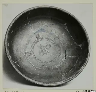 Black glazed bowl photographed from above, its interior decorated with a central palmette design and a ring of tongue-shaped motifs.