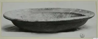 Pottery Red Slip bowl, shallow with a wide flat rim, seen from the side on a pale surface