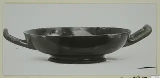 Black glazed bowl with two horizontal handles and a low foot, photographed on a plain background.