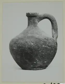 Single-handled pottery jug from the Marion tomb finds, photographed against a plain pale background.