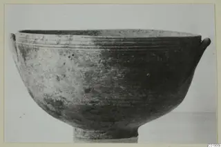 Pottery bowl with a ring foot and two small handles on the rim, photographed against a plain background