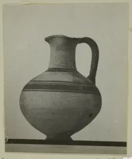 Pottery jug with a high loop handle and dark painted bands on the shoulder and body, shown against a grey backdrop.