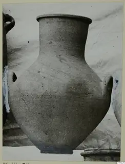 Large plain pottery vessel with two handles and a flat rim, photographed against a pale cloth backdrop