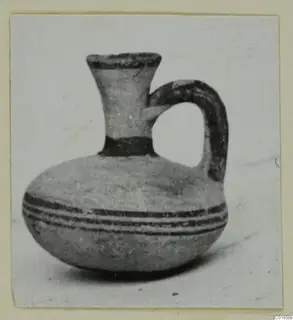 Small jug with a flaring neck, single loop handle and dark painted bands, photographed on a pale background.