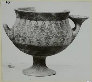 Pottery White Painted I bowl with a lozenge pattern, two handles and a footed base, seen from the side.