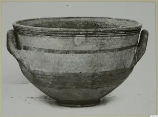 Pottery bowl with two loop handles and horizontal painted bands, photographed on a plain surface