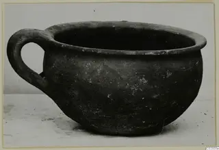 Coarse ware cup with a single loop handle, photographed on a pale surface.