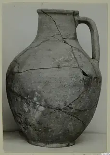 Plain pottery jug with a single loop handle and a broad rim, shown with visible cracks and repairs.