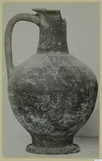 Pottery jug with a loop handle, tall neck and ring foot, photographed against a plain background