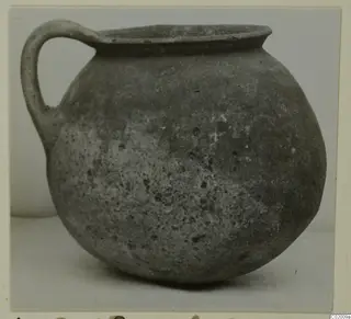 Coarse ware jug with a single loop handle and a rounded body, photographed against a plain background.