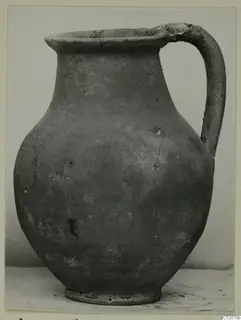 Plain pottery jug with a single loop handle, shown against a pale backdrop.