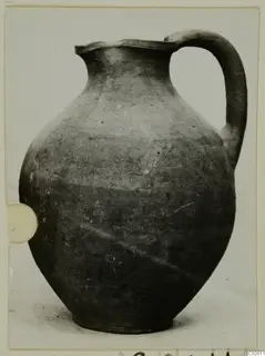 Pottery jug from Vouni with one handle and a plain grey-brown surface, photographed on a pale background.