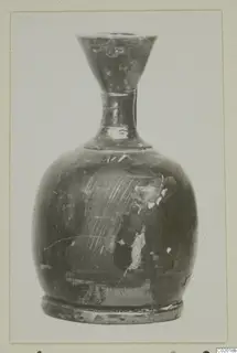 Dark pottery vessel with a flared mouth, narrow neck and ring foot, with pale lines on one side