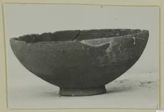 Footed pottery bowl with a broken, uneven rim, shown in side view against a pale background
