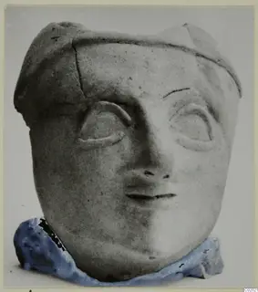 Head of a figure with large raised-rimmed eyes and a cap-like headdress, standing in blue modelling clay