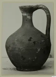 Plain pottery jug with a high loop handle and a rounded body, photographed on a pale surface.