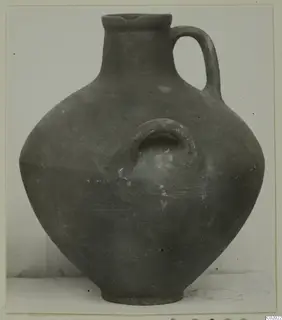 Coarse ware jug with a loop handle and a small loop lug on the body, photographed against a plain background.
