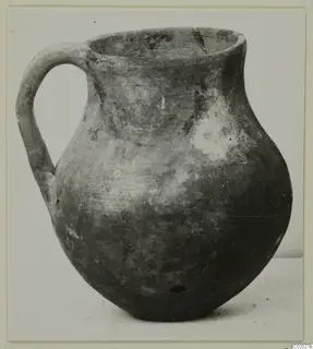 Coarse ware jug with a strap handle and rounded body, photographed on a plain surface