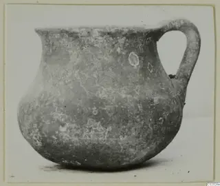 Pottery jar with a single loop handle and a rounded body, photographed against a plain background