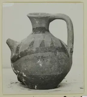 Pottery White Painted VI jug with a spout, strap handle and dark painted bands, shown on a plain surface