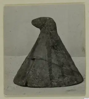 Cone-shaped object with a rounded knob at the top, photographed on a pale surface against a plain backdrop