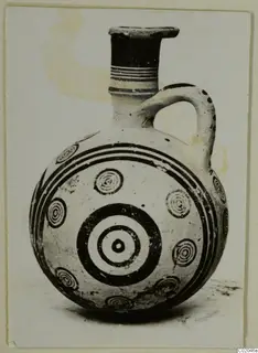 Pottery juglet with black concentric circles and bands on a pale body, photographed against a plain background