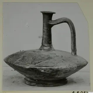 Pottery jug with a tall flared neck, a single loop handle and a flattened, ribbed body on a low foot.