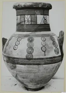 White Painted IV amphora with two handles, concentric circle motifs and painted bands, standing on a pale surface