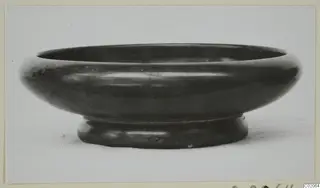 Black Glazed Ware bowl with a wide rounded body and a short ring foot, seen from the side