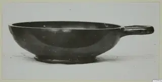 Black glazed bowl with a single horizontal handle, seen from the side.