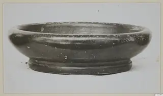 Black glazed ware bowl with a wide rounded body and ring foot, seen from the side.