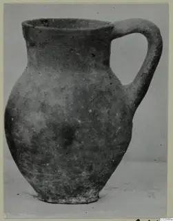 Pottery jug with a single loop handle, shown from the side against a plain grey backdrop.